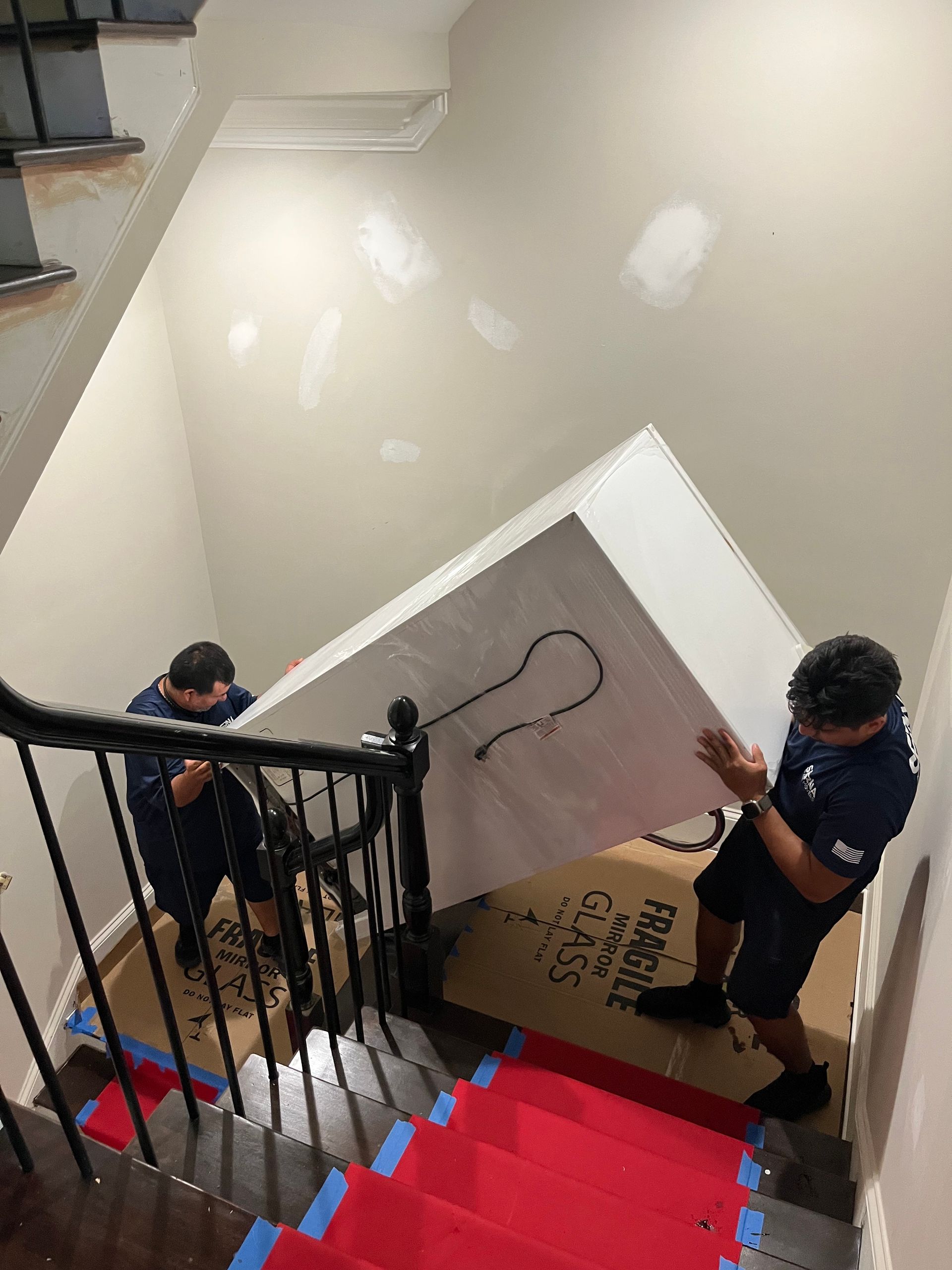 Two men are carrying a large white box up a set of stairs.