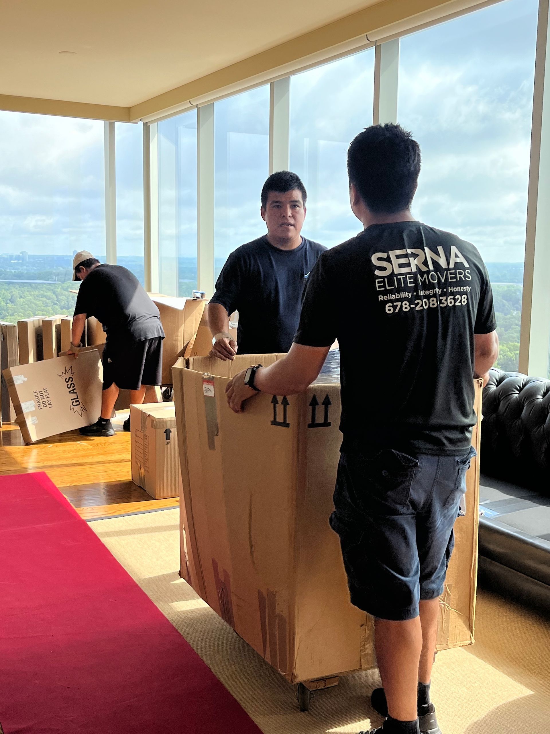 Two men are moving a large cardboard box in a living room.