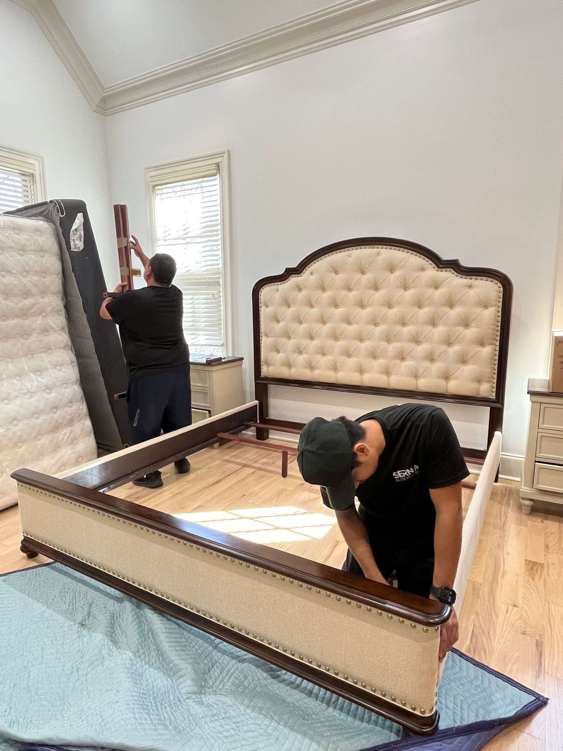 Two men are moving a bed in a bedroom.