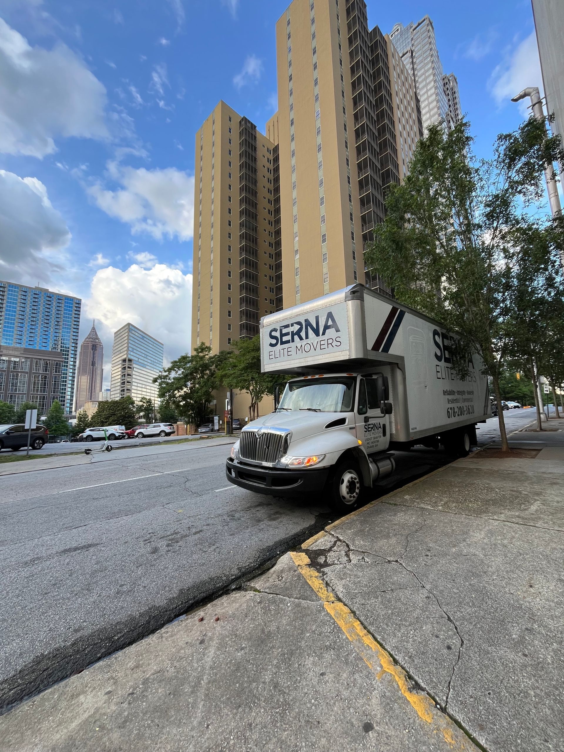 A moving truck is parked on the side of the road in front of tall buildings.