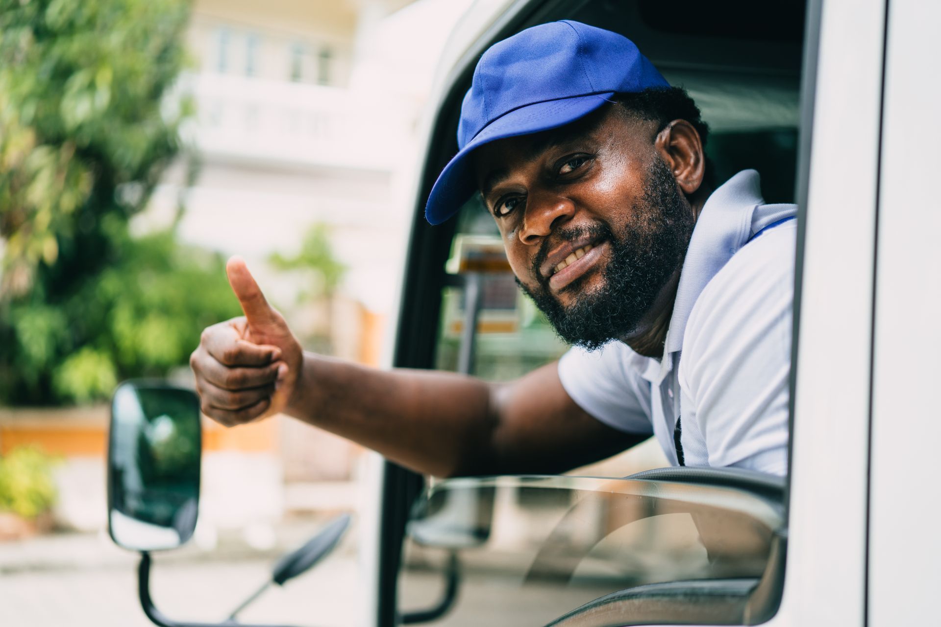 Man in blue cap gives thumbs up from a vehicle window.