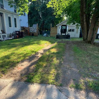 A dirt road leading to a house with a tractor in the backyard.