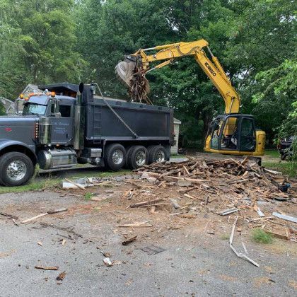 A dump truck is being loaded with wood by an excavator.