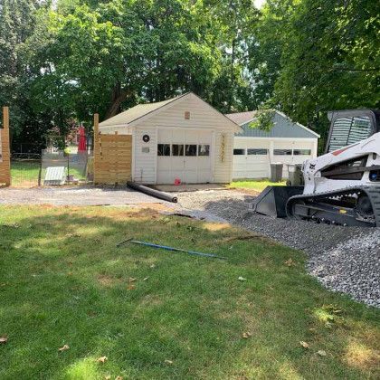 A bulldozer is moving gravel in a yard in front of a garage.