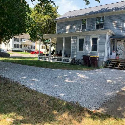 A house with a porch and a gravel driveway in front of it.