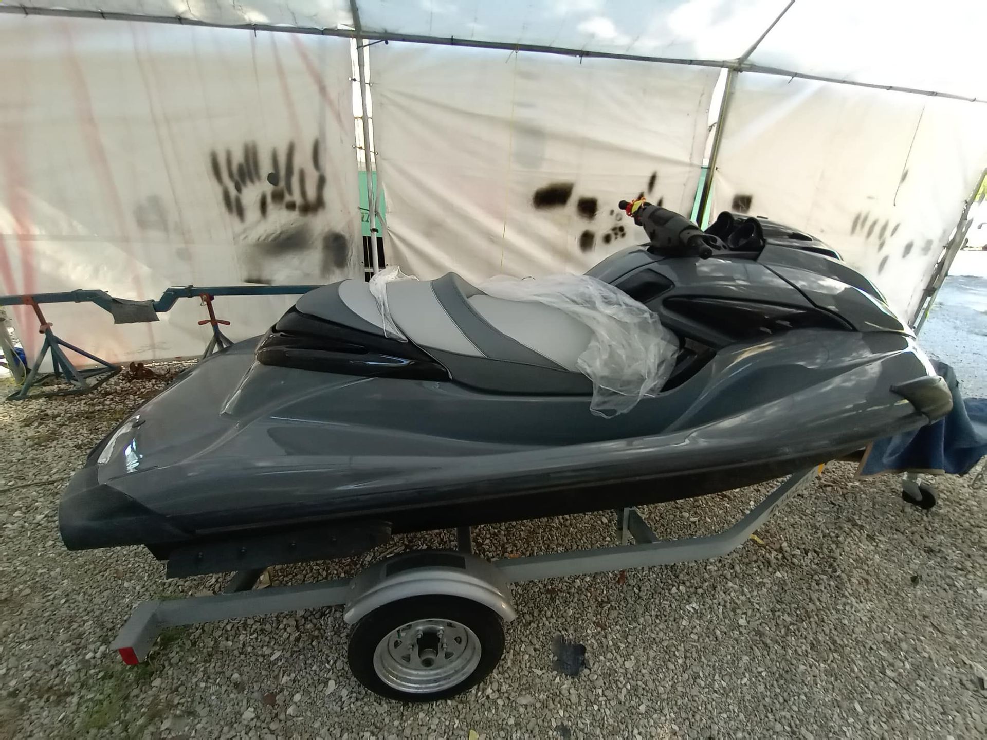 Dark gray jet ski on a trailer, parked under a tarp.