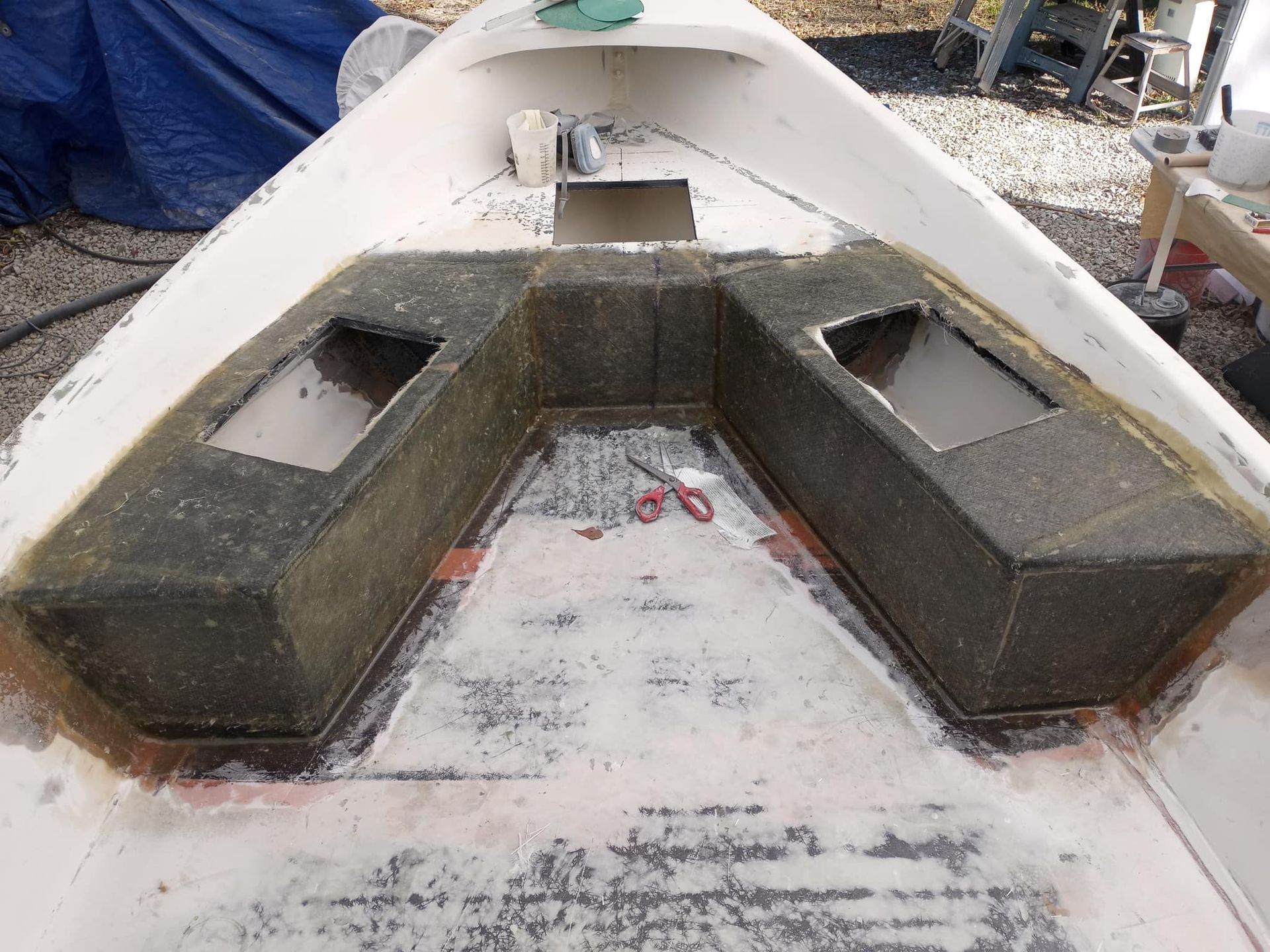 Boat interior with a U-shaped seating structure. Grey foam seating, white boat interior. Scissors lie in the center.