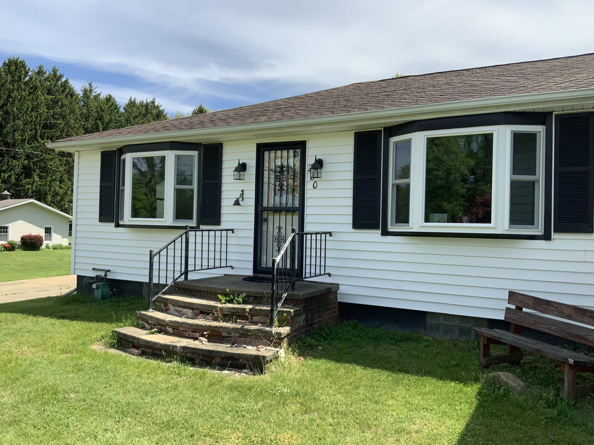 A white house with black shutters and a bench in front of it.