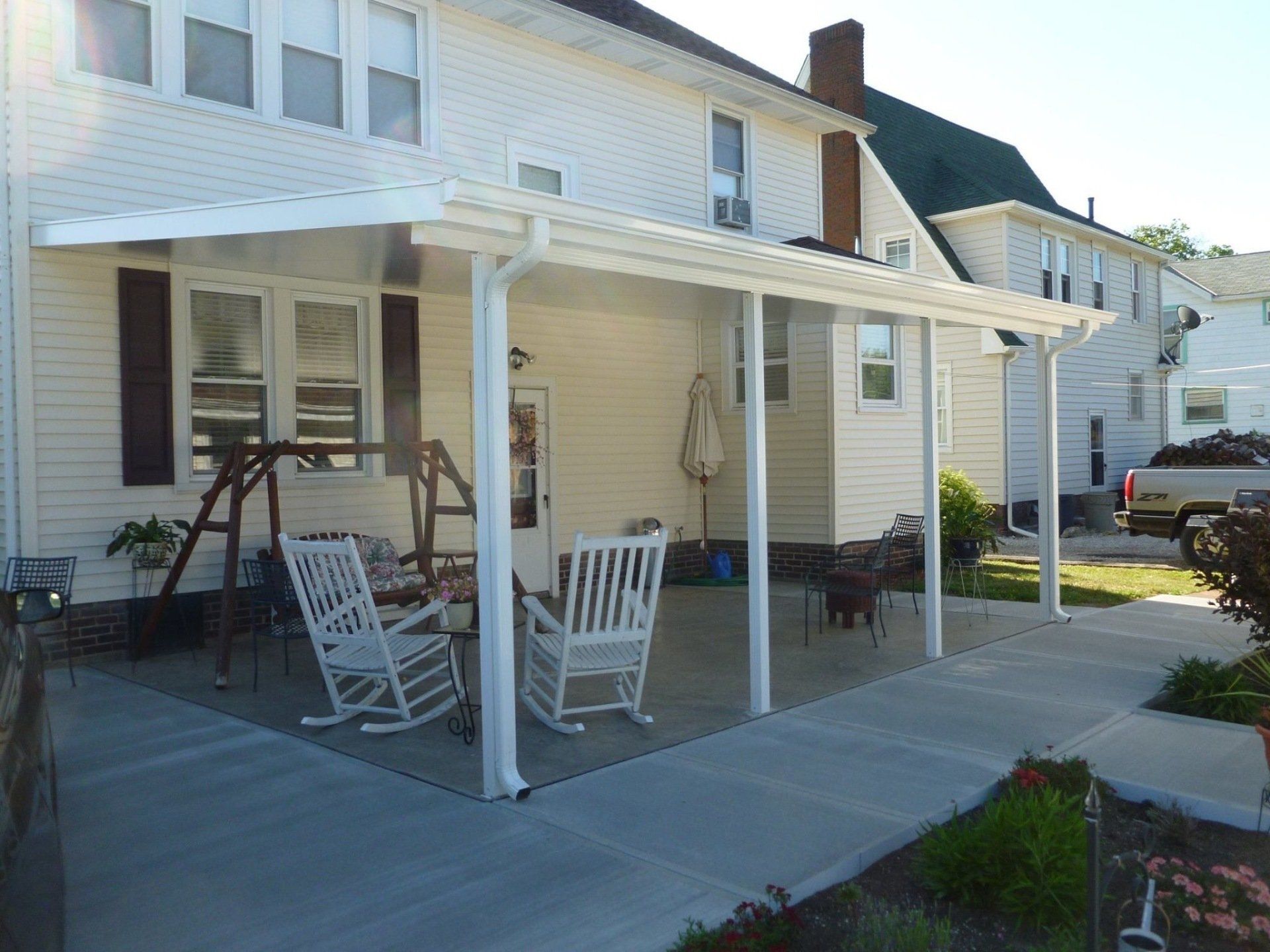 A white house with a porch with rocking chairs and a table.