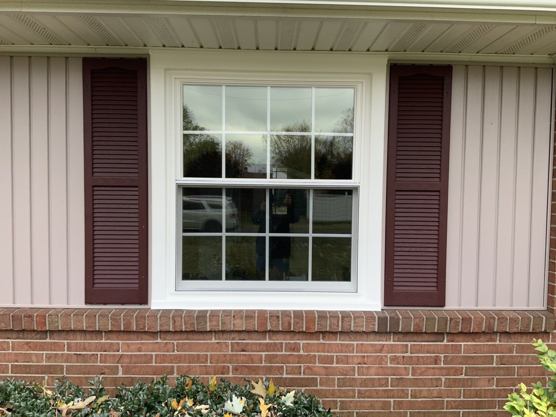 A white window with burgundy shutters on a brick house.