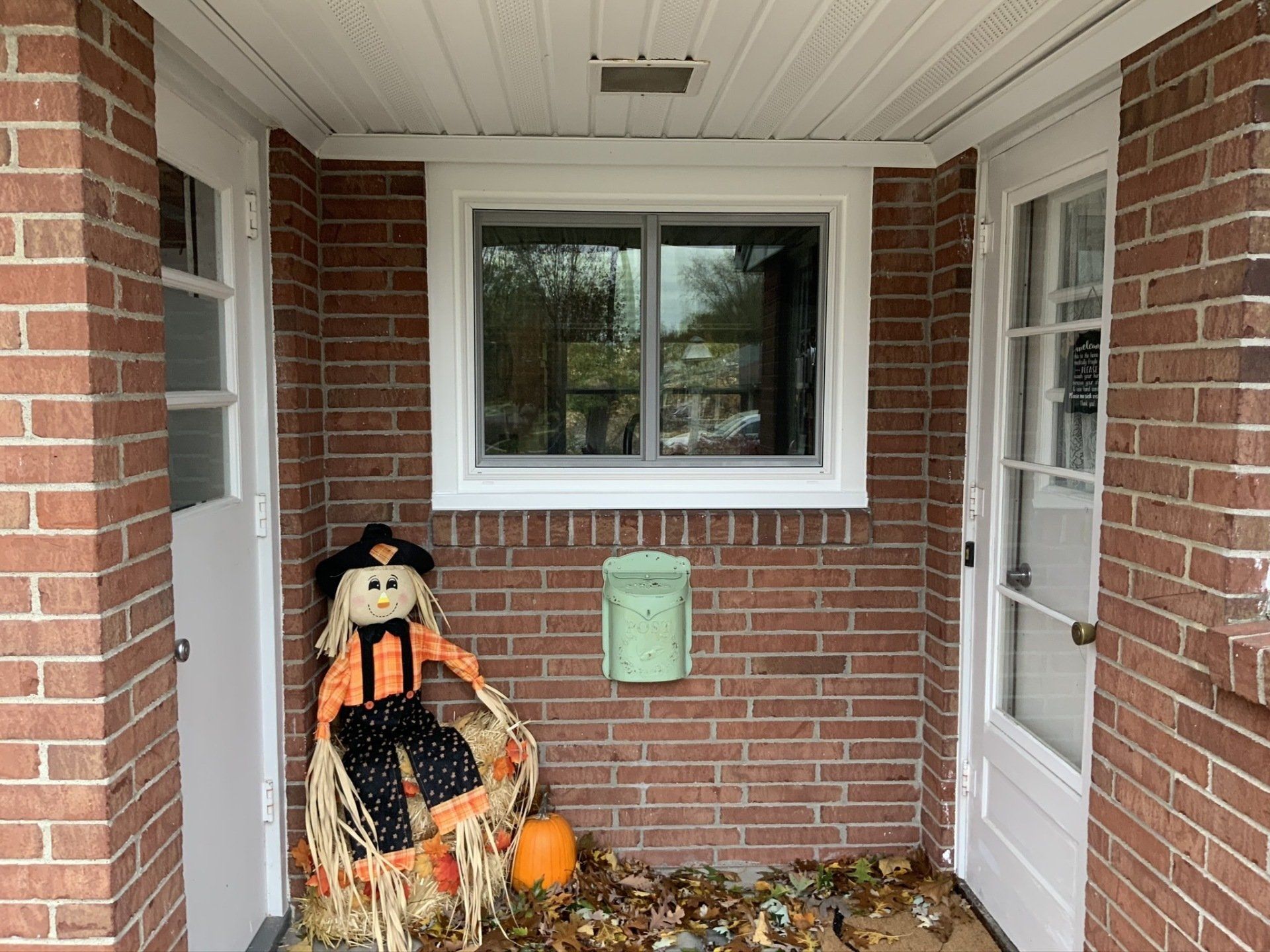 A scarecrow is on the porch of a brick house.