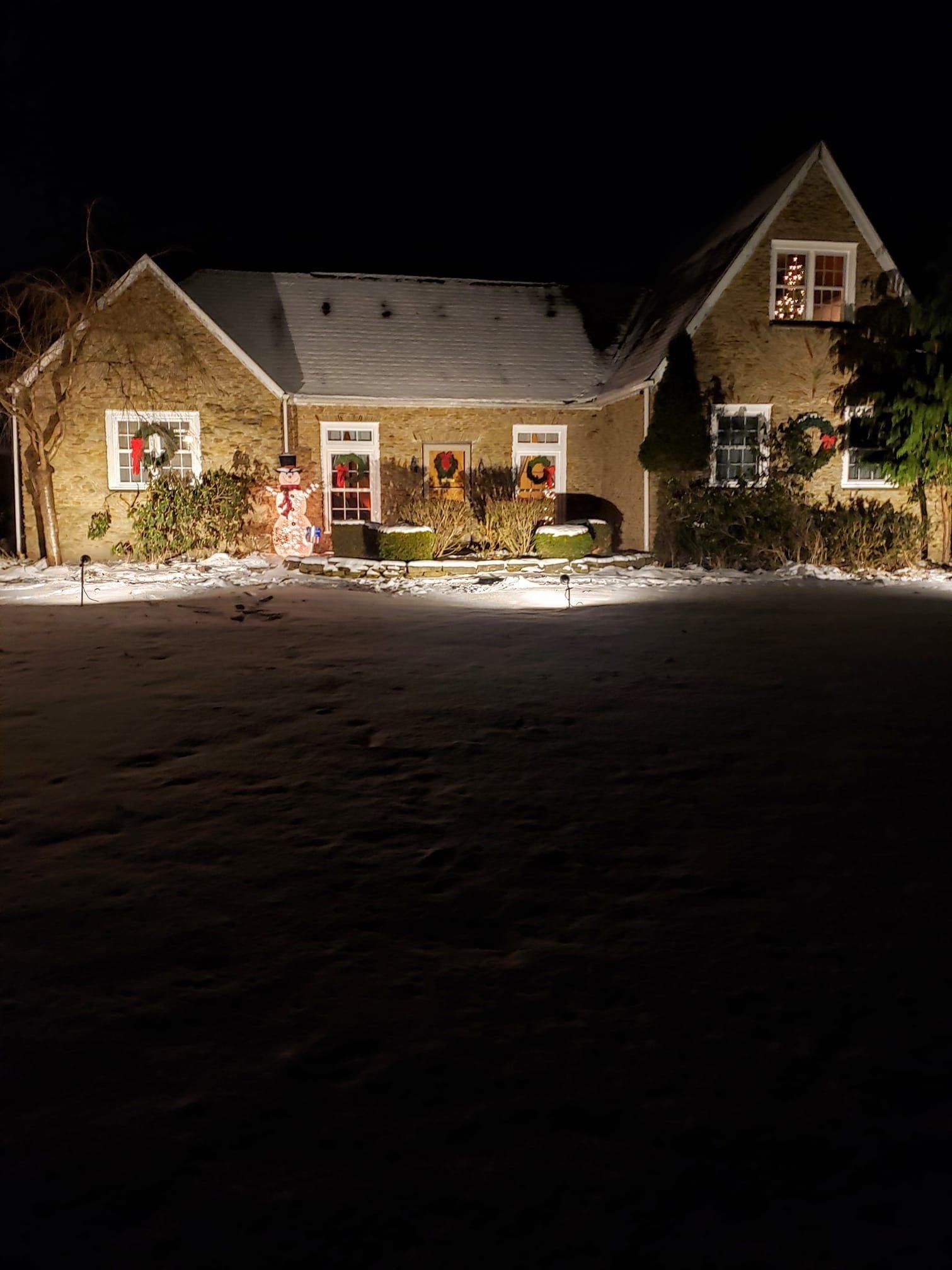 A house decorated for christmas is lit up at night in the snow.