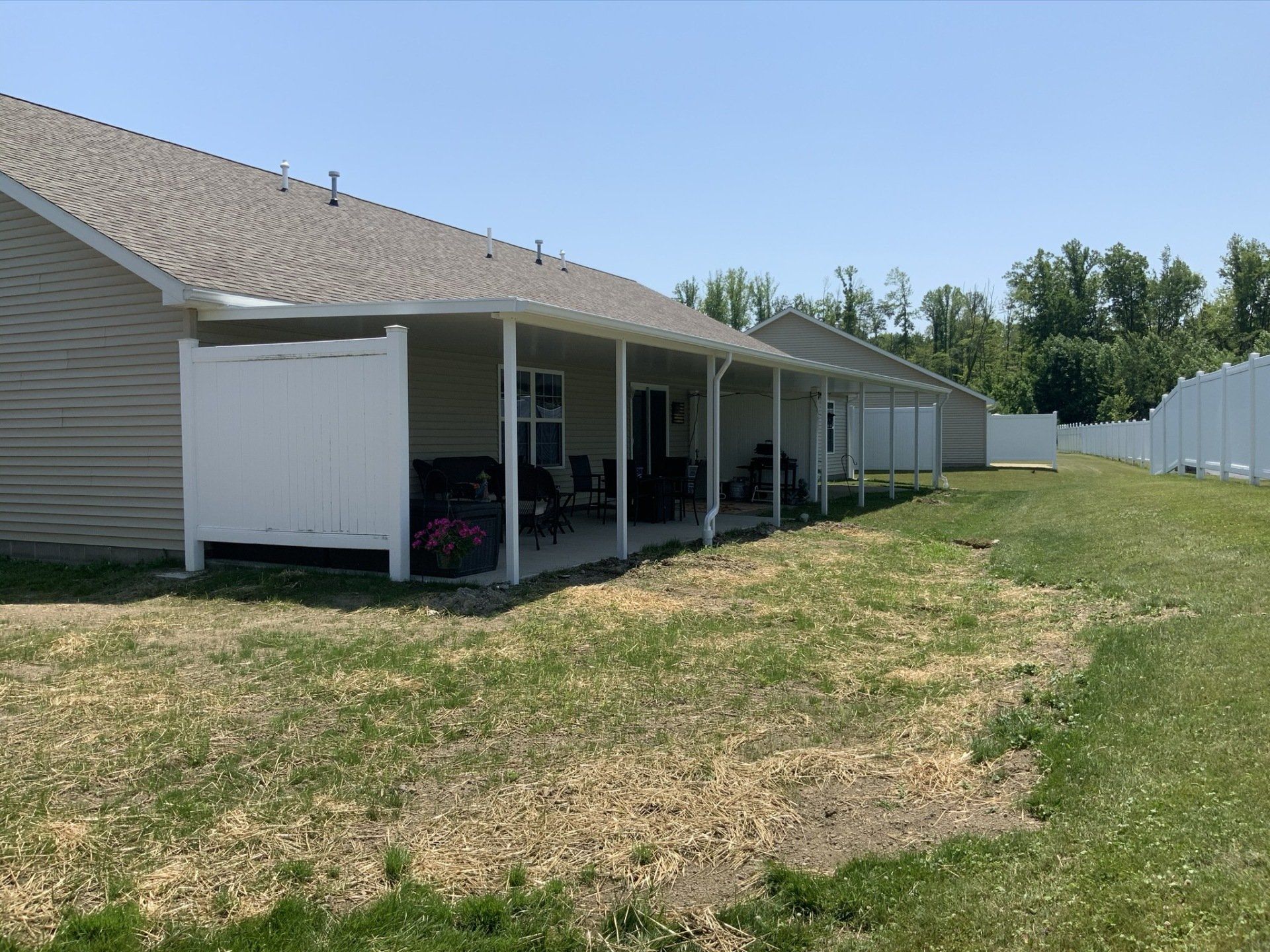 The backyard of a house with a covered porch and a white fence.