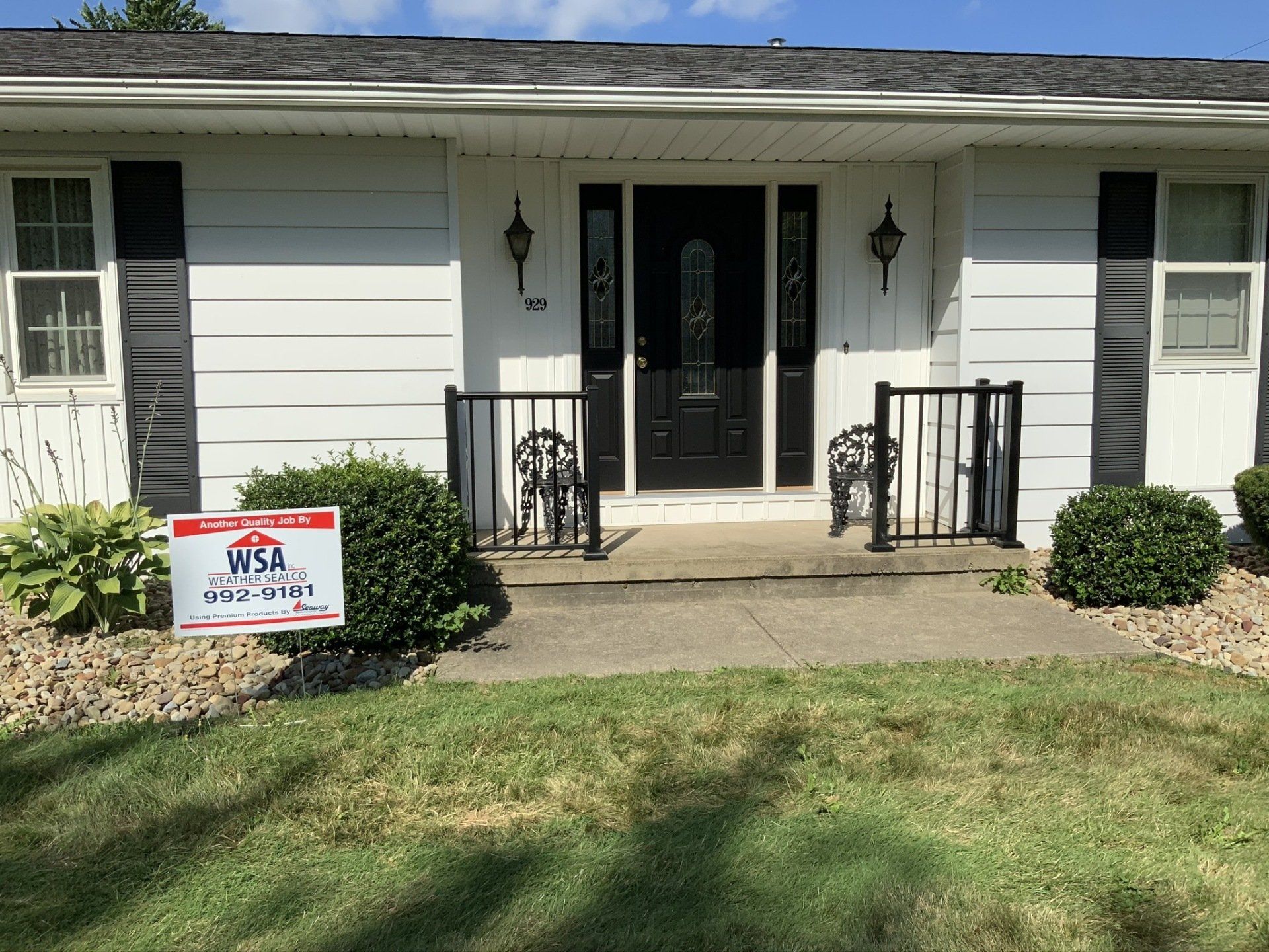 A white house with black shutters and a for sale sign in front of it.