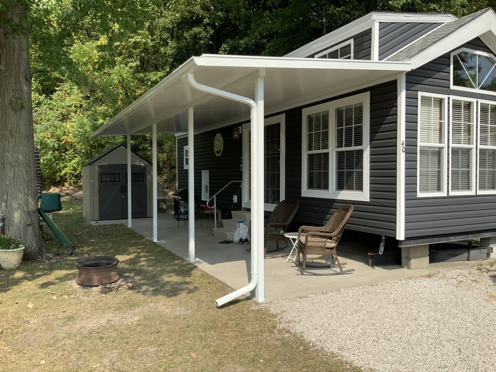 A small black house with a white porch and chairs.