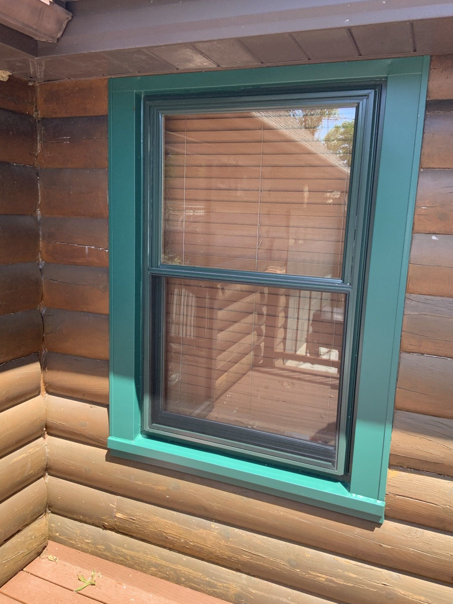 A window on the side of a log cabin with a green trim.