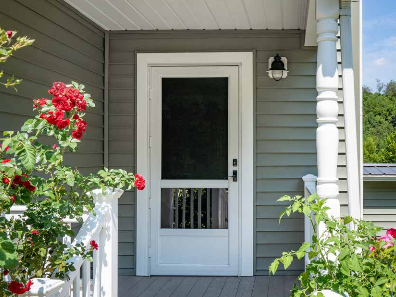 A white screen door is on the porch of a house.