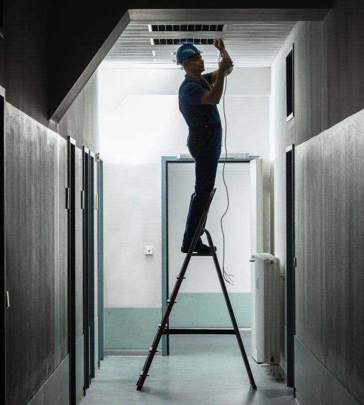 Un homme est debout sur une échelle et travaille sur un ventilateur de plafond
