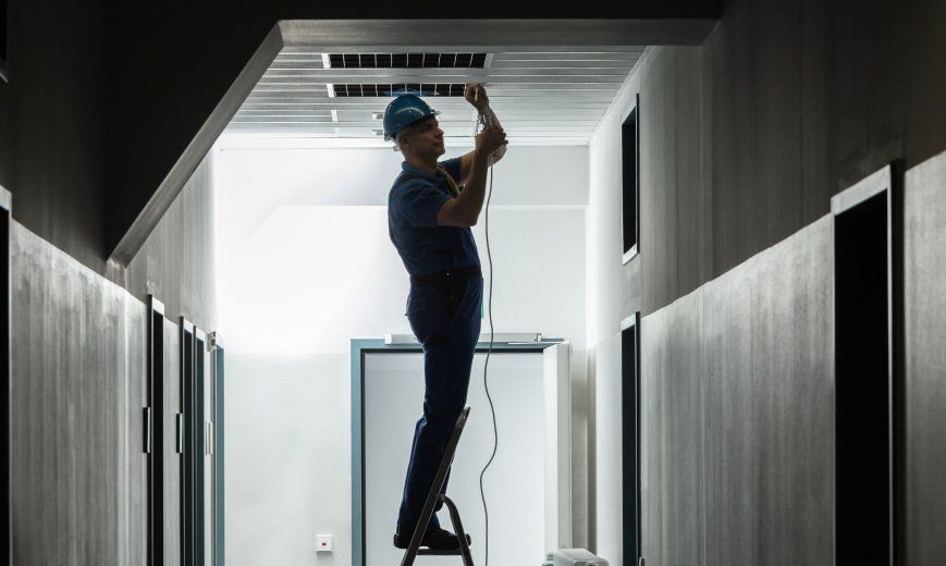 Un homme se tient debout sur une échelle et répare un luminaire dans un couloir.