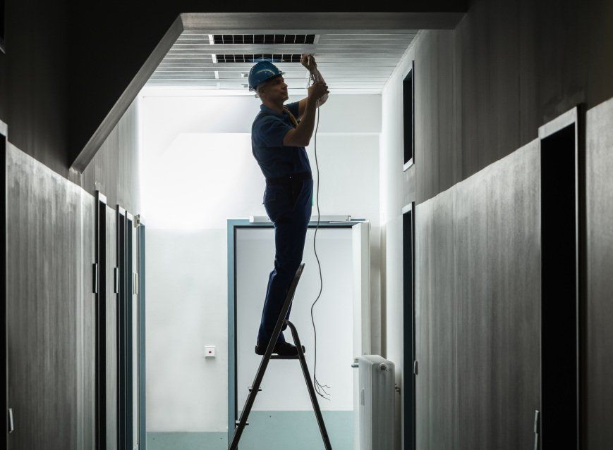 Un homme est debout sur une échelle et répare un climatiseur dans un couloir.