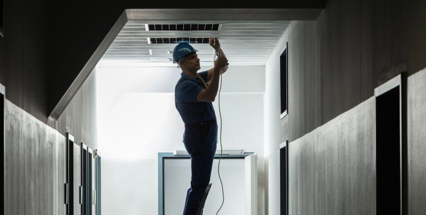 Un homme travaille sur un luminaire dans un couloir.