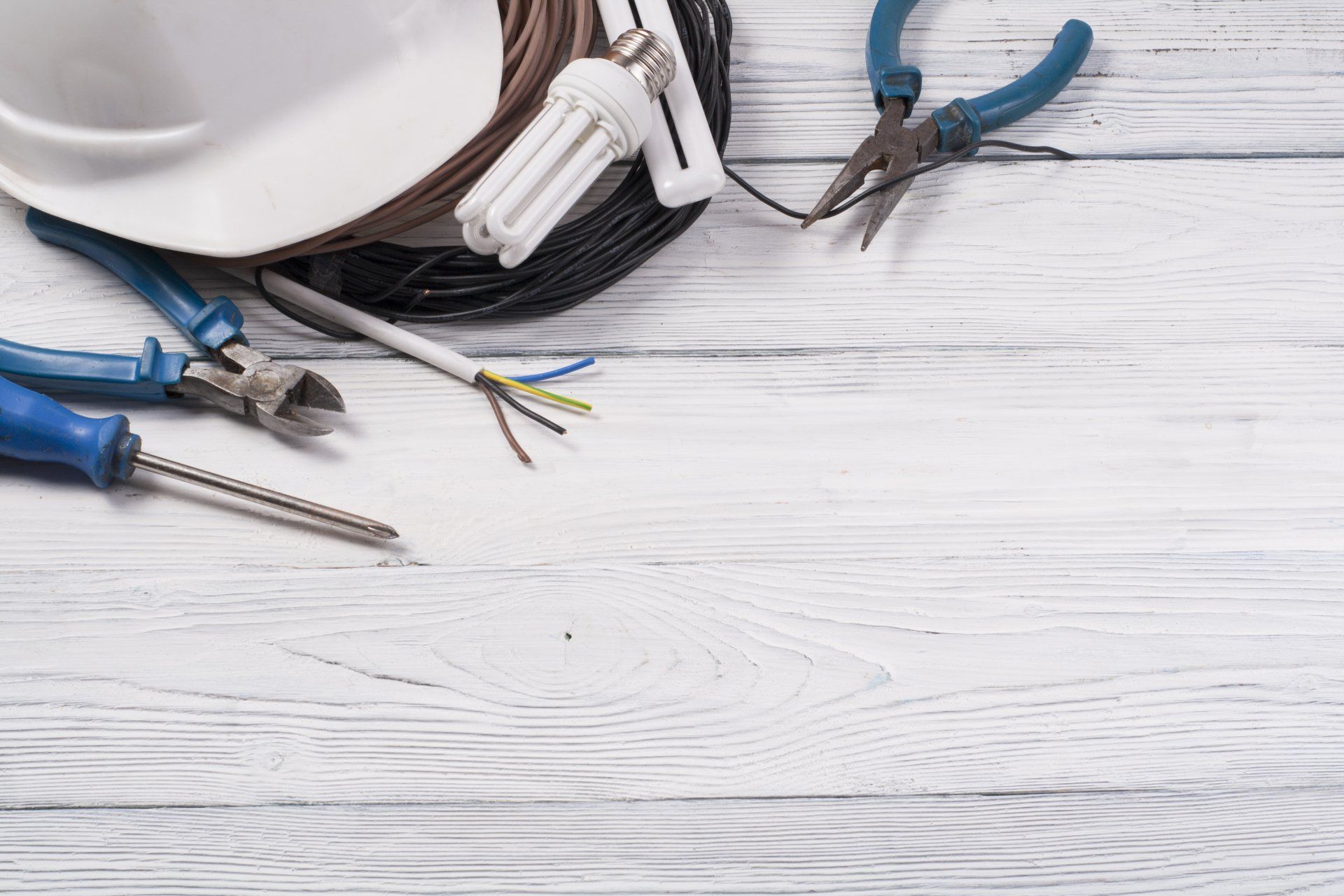 Un casque, un tournevis, une pince, un fil et une ampoule sont sur une table en bois.