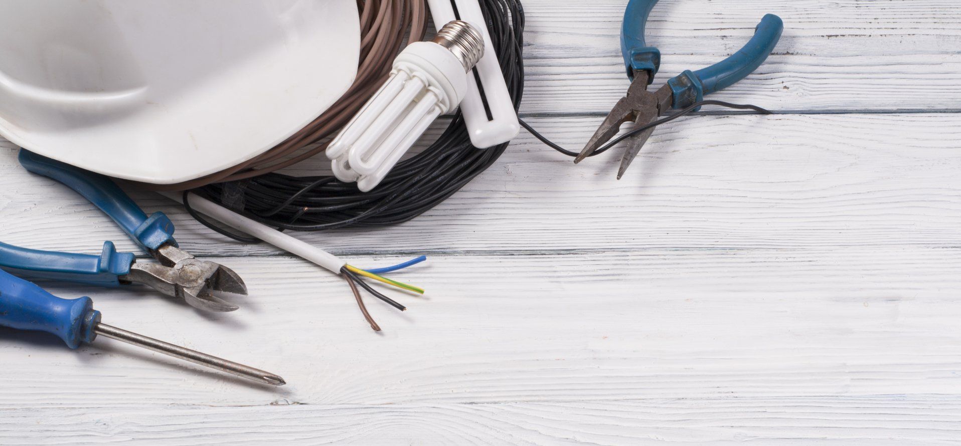 Une bobine de fil, une ampoule, une pince et un tournevis sont sur une table en bois.