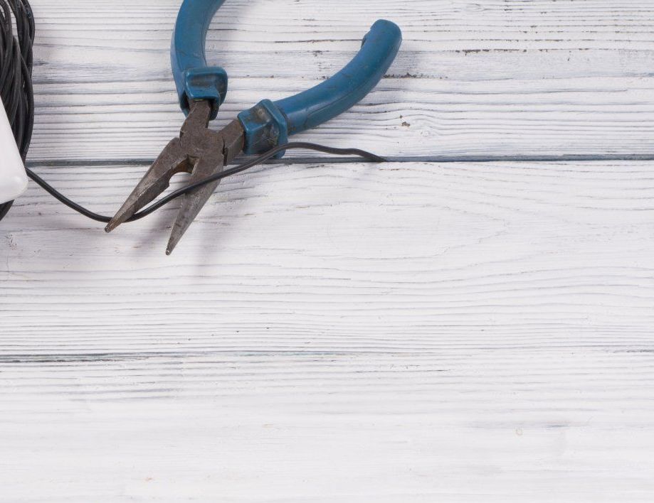 Pince bleue coupant un fil noir sur une surface en bois blanche.