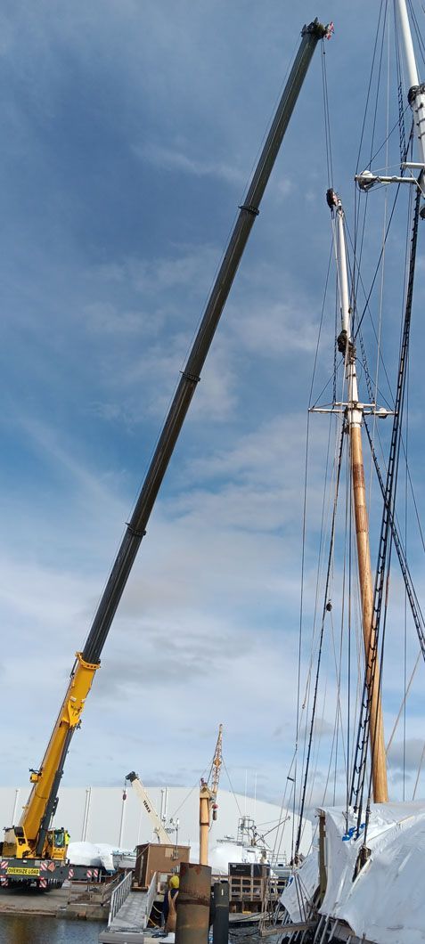 A large yellow crane is lifting a sailboat in the water.