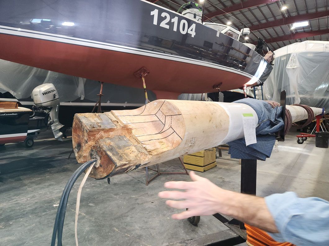 A person is holding a piece of wood in front of a boat with the number 12104 on it.