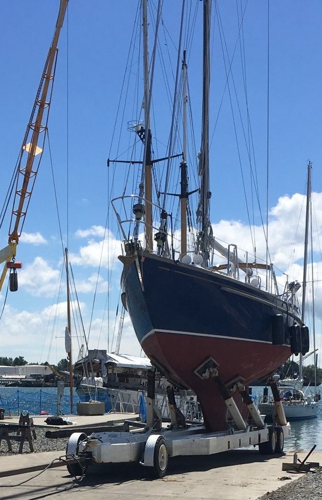 A large sailboat is being lifted into the water by a crane.