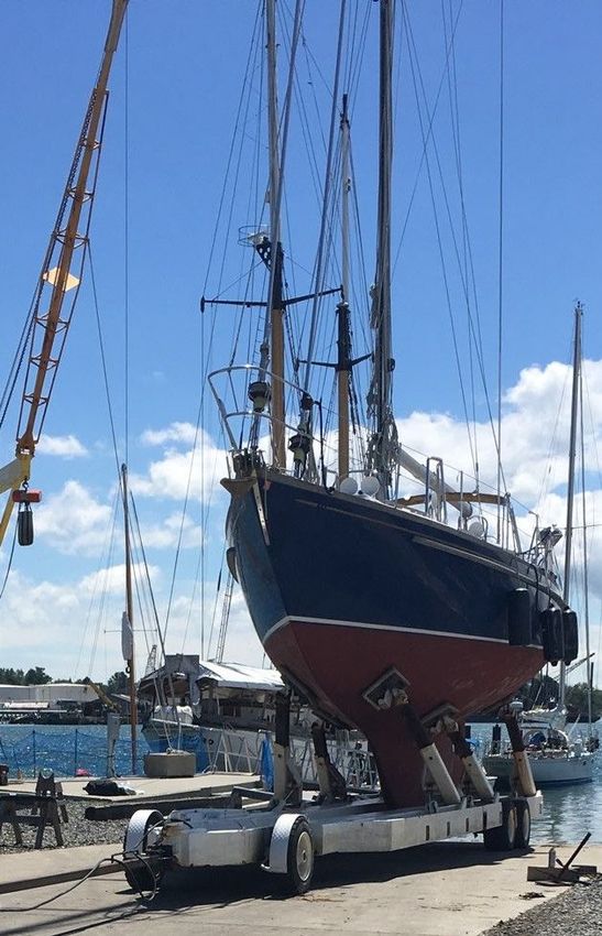 A large sailboat is being lifted into the water by a crane.