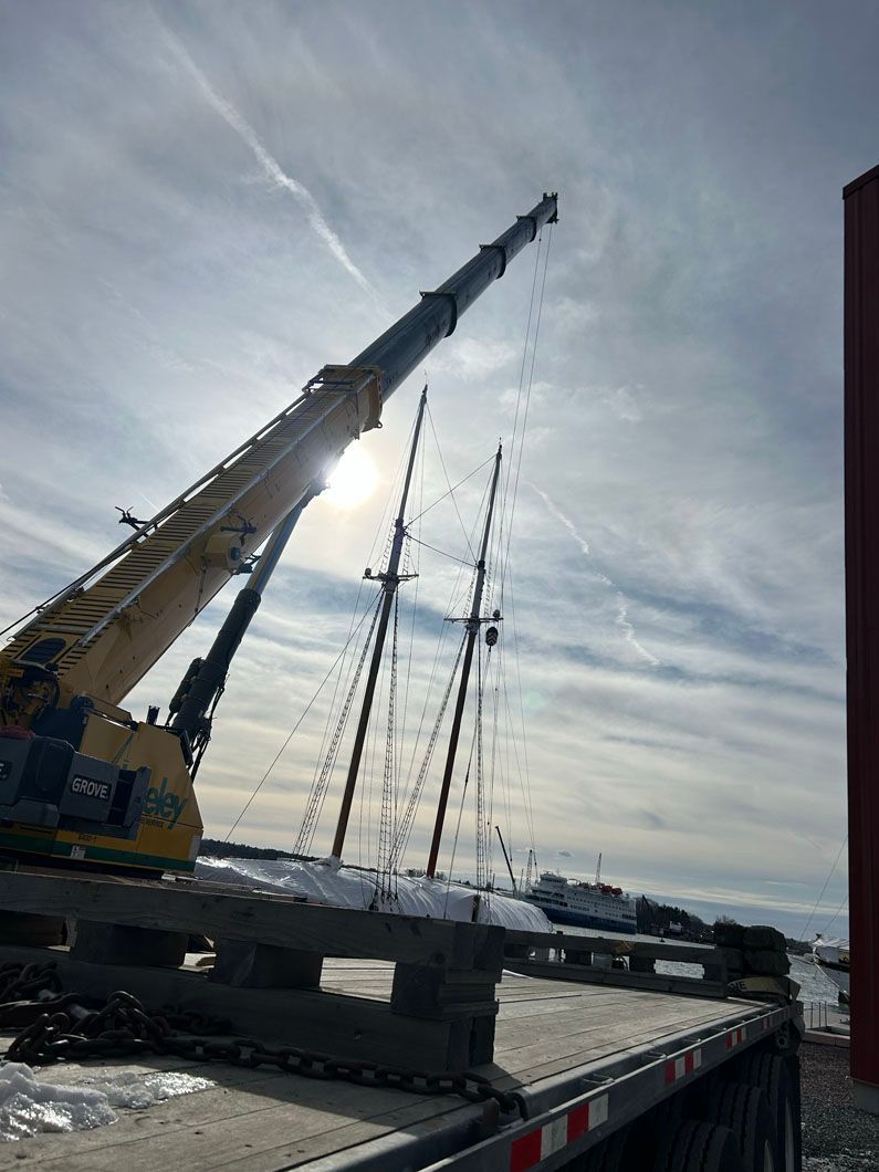 A large crane is sitting on top of a trailer next to a boat.