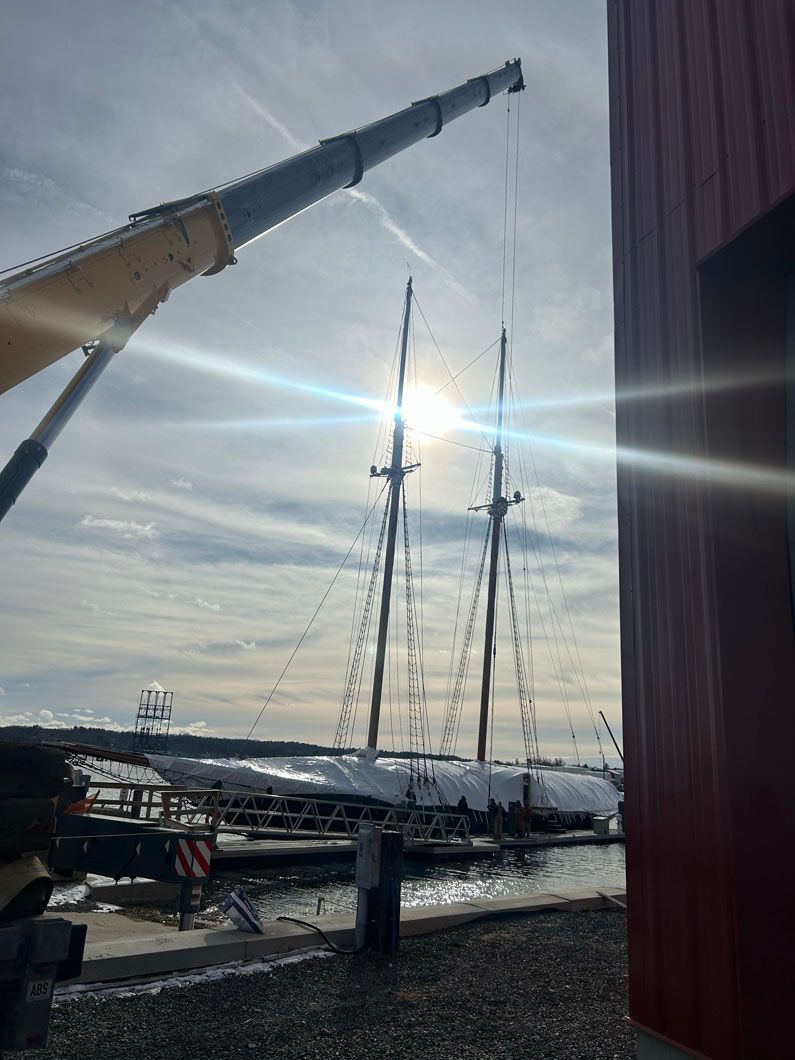 A crane is lifting a large sailboat in the water.