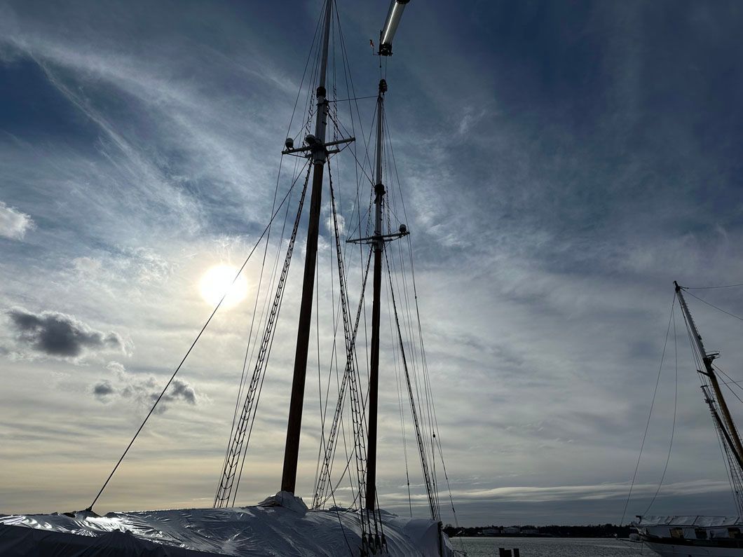 A sailboat is docked in the water with the sun shining through the clouds.
