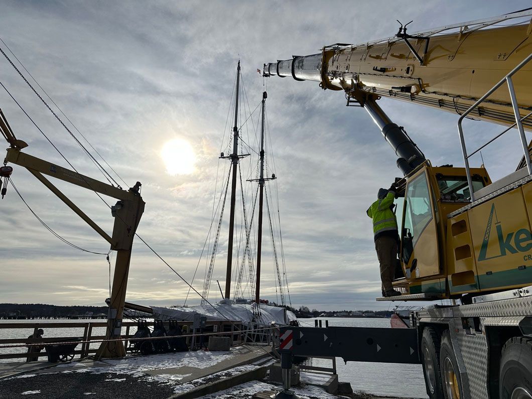 A large yellow crane is lifting a sailboat into the water.