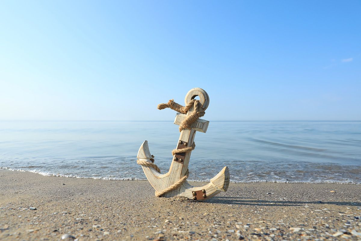 An anchor is sitting on the beach near the ocean.