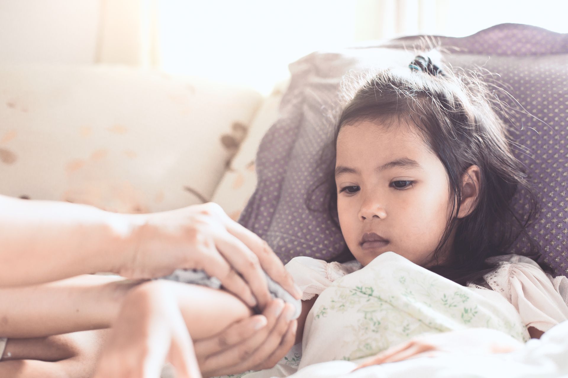 A caregiver comforting a young girl in bed, showing care during a childhood illness. 
