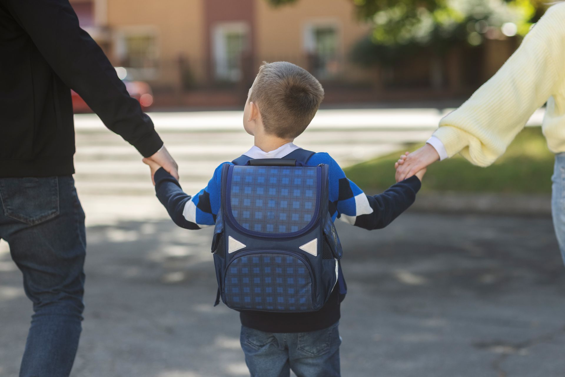  A child holding hands with parents, walking outside on the way to school.