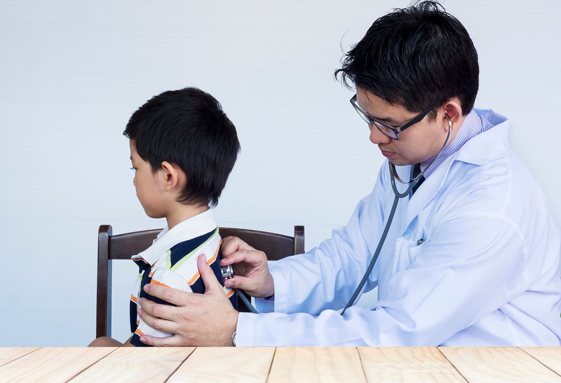 A doctor using a stethoscope to examine a young boy and check for common childhood illnesses.