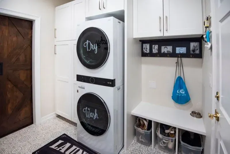 Laundry room with stacked washer and dryer, white cabinets, bench, and shoe storage.