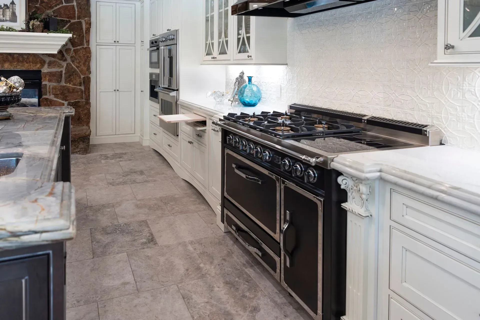 A luxurious kitchen with a black stove, white cabinets, and stone countertops.