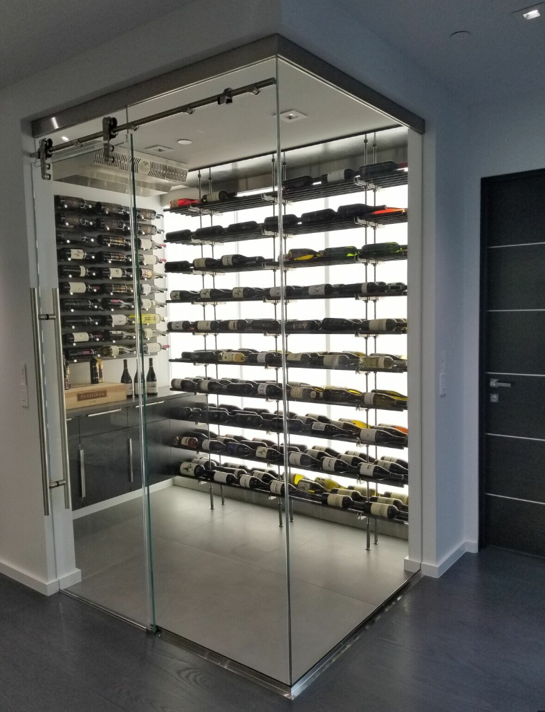 Glass-enclosed wine cellar with sliding door, filled with bottles, illuminated.