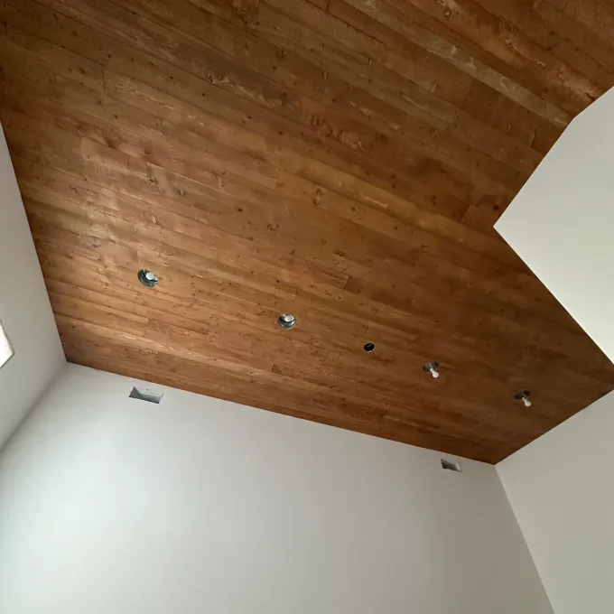 Wooden plank ceiling with recessed lights, above white walls.