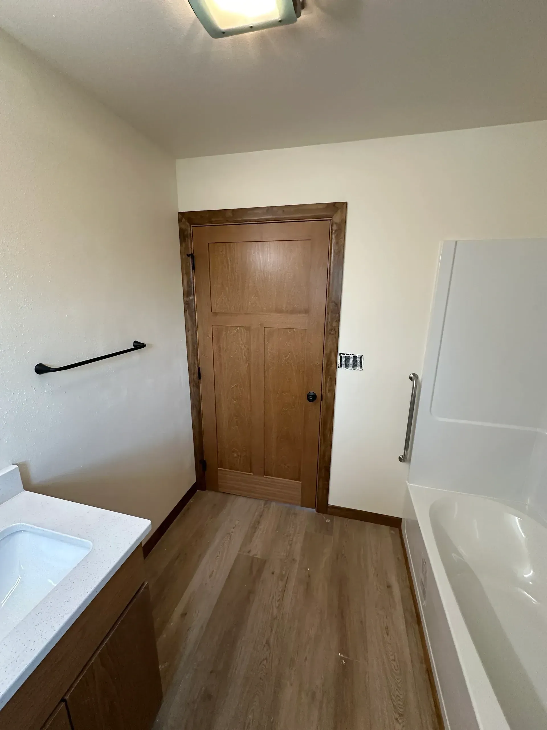 Bathroom with light wood door, vanity with white sink, and bathtub.