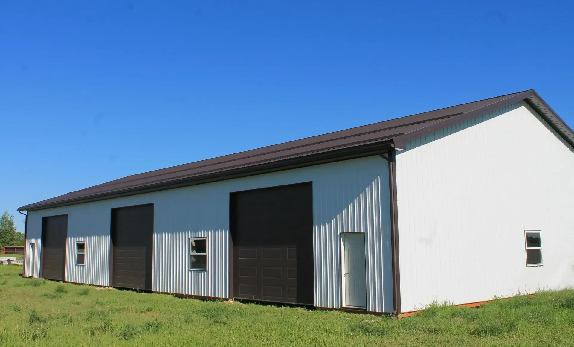 White metal building with brown doors and roof against a blue sky.