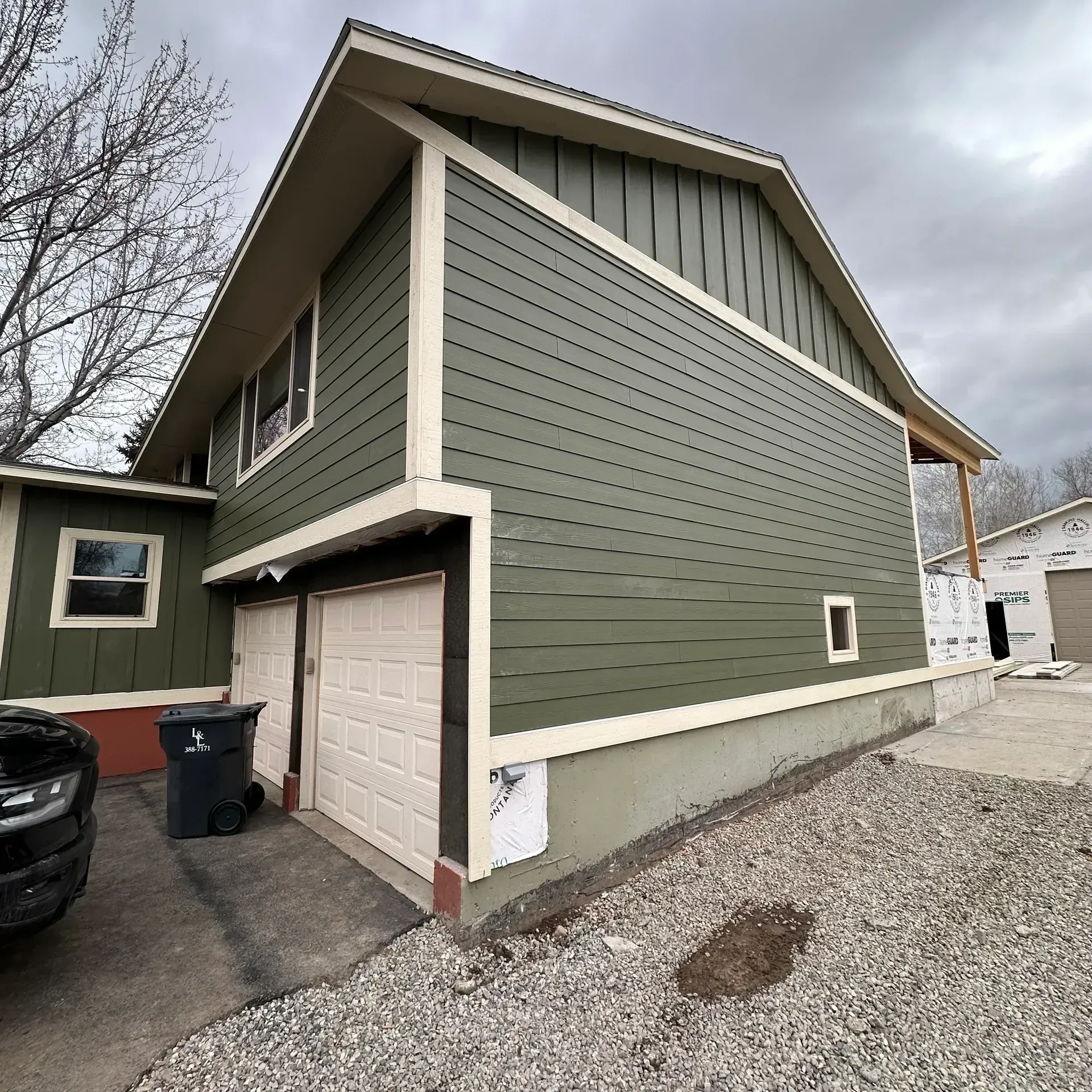 Two-story house with green siding, white trim, and garage doors. Cloudy day.