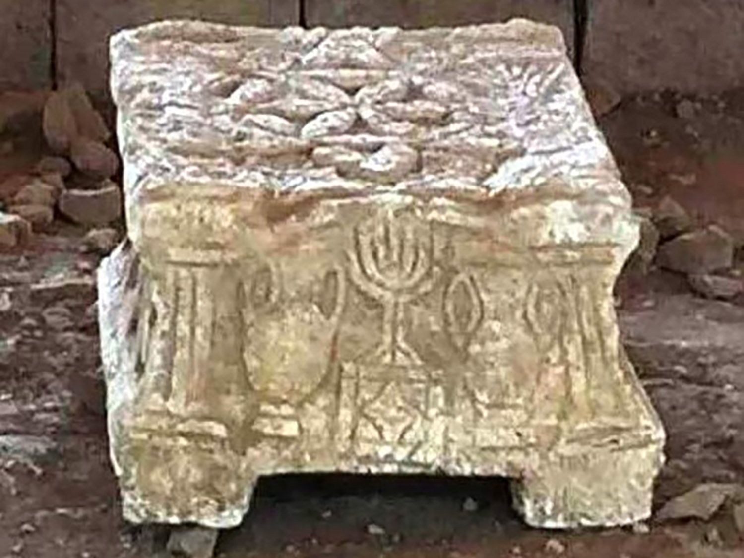 A stone statue with a menorah on it is sitting on the ground.