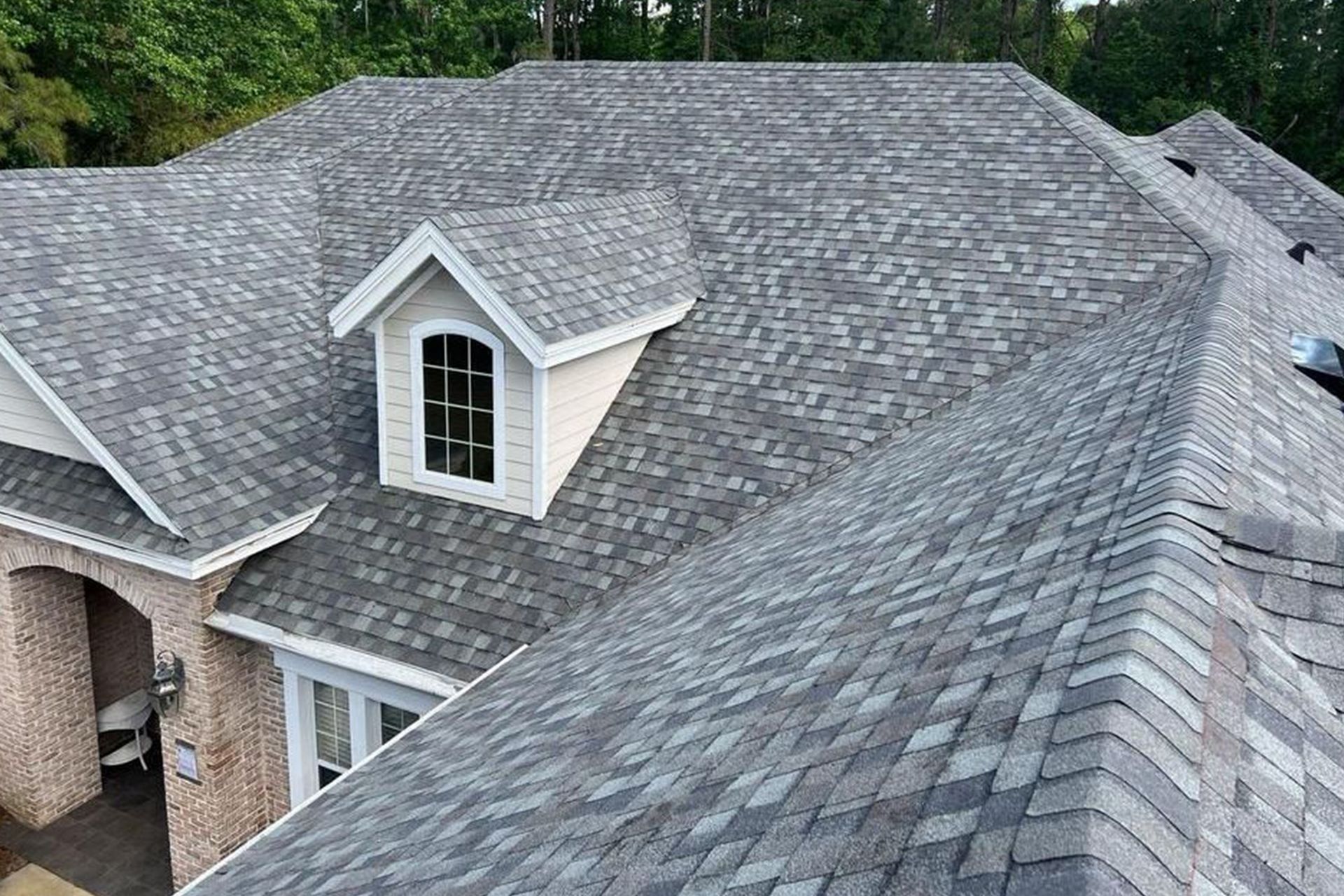 Gray shingle roof on a house with a dormer and light-colored brick exterior.