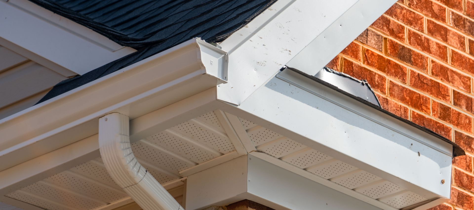 White gutters and soffit on a brick building with a dark roof.